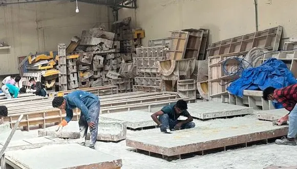 Workers finishing GRC panels on casting tables, with the mould store behind