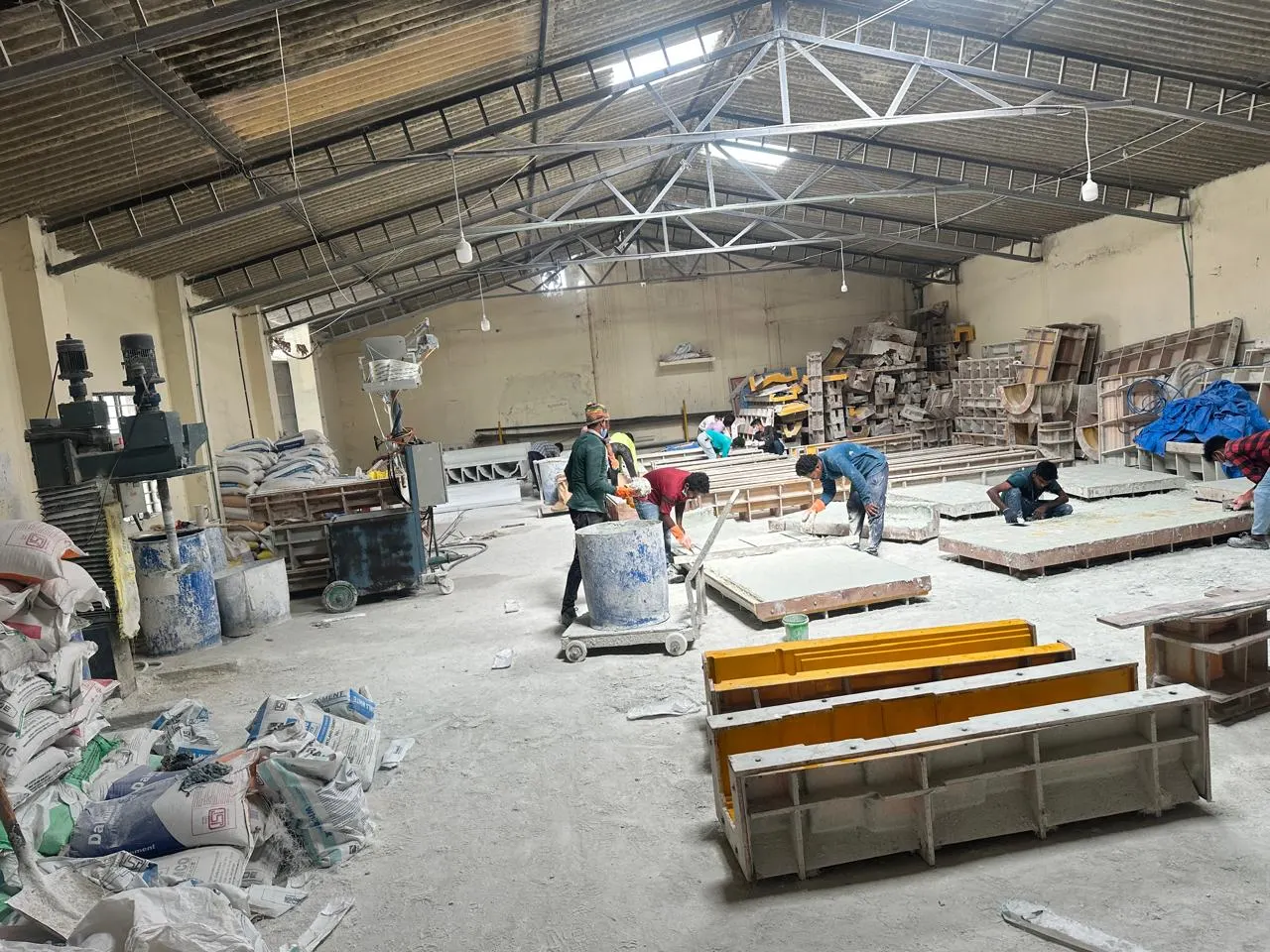 The GRC casting hall in Bangalore: workers finishing flat panels on casting tables, with yellow cornice profile moulds in front and stacked moulds at the back